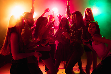 Image showing A crowd of people in silhouette raises their hands on dancefloor on neon light background