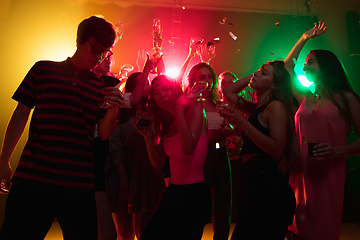 Image showing A crowd of people in silhouette raises their hands on dancefloor on neon light background