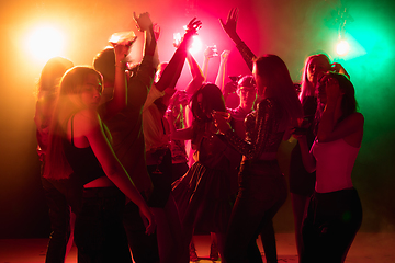 Image showing A crowd of people in silhouette raises their hands on dancefloor on neon light background