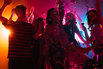 Image showing A crowd of people in silhouette raises their hands on dancefloor on neon light background