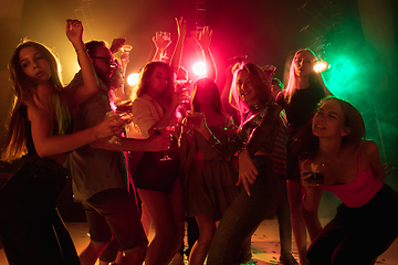 Image showing A crowd of people in silhouette raises their hands on dancefloor on neon light background