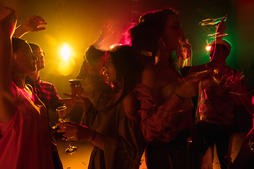 Image showing A crowd of people in silhouette raises their hands on dancefloor on neon light background