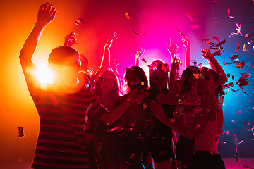 Image showing A crowd of people in silhouette raises their hands on dancefloor on neon light background