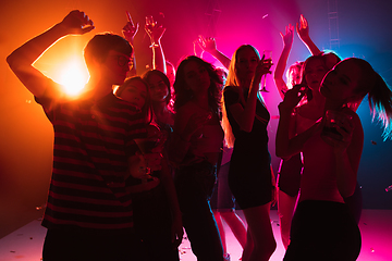 Image showing A crowd of people in silhouette raises their hands on dancefloor on neon light background