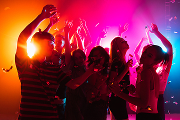 Image showing A crowd of people in silhouette raises their hands on dancefloor on neon light background