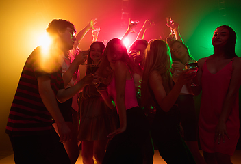 Image showing A crowd of people in silhouette raises their hands on dancefloor on neon light background