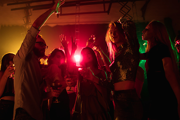 Image showing A crowd of people in silhouette raises their hands on dancefloor on neon light background