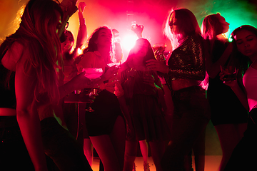 Image showing A crowd of people in silhouette raises their hands on dancefloor on neon light background