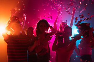 Image showing A crowd of people in silhouette raises their hands on dancefloor on neon light background