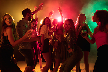 Image showing A crowd of people in silhouette raises their hands on dancefloor on neon light background