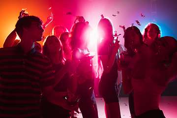 Image showing A crowd of people in silhouette raises their hands on dancefloor on neon light background