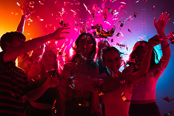 Image showing A crowd of people in silhouette raises their hands on dancefloor on neon light background