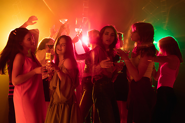 Image showing A crowd of people in silhouette raises their hands on dancefloor on neon light background