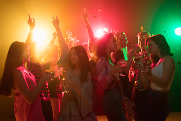 Image showing A crowd of people in silhouette raises their hands on dancefloor on neon light background