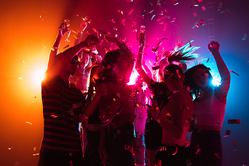 Image showing A crowd of people in silhouette raises their hands on dancefloor on neon light background