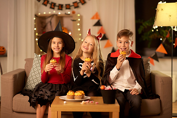 Image showing kids in halloween costumes eating cupcakes at home