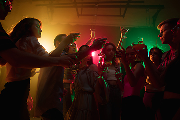 Image showing A crowd of people in silhouette raises their hands on dancefloor on neon light background