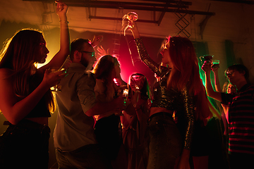 Image showing A crowd of people in silhouette raises their hands on dancefloor on neon light background