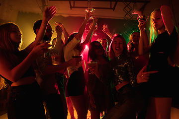 Image showing A crowd of people in silhouette raises their hands on dancefloor on neon light background