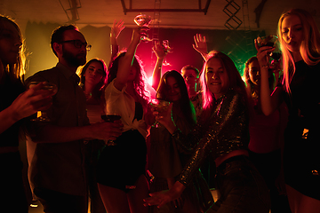 Image showing A crowd of people in silhouette raises their hands on dancefloor on neon light background