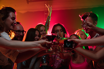 Image showing A crowd of people in silhouette raises their hands on dancefloor on neon light background