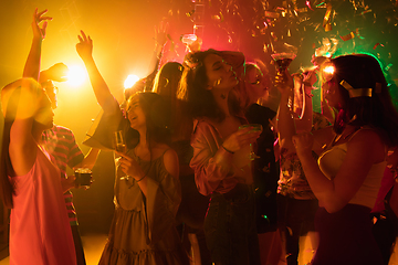 Image showing A crowd of people in silhouette raises their hands on dancefloor on neon light background