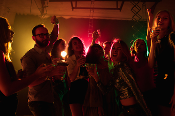 Image showing A crowd of people in silhouette raises their hands on dancefloor on neon light background