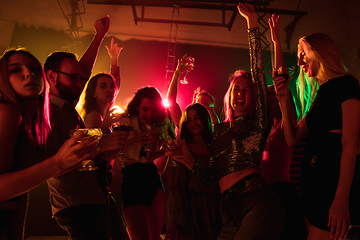 Image showing A crowd of people in silhouette raises their hands on dancefloor on neon light background