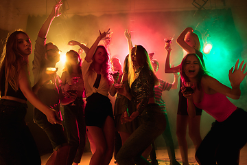 Image showing A crowd of people in silhouette raises their hands on dancefloor on neon light background