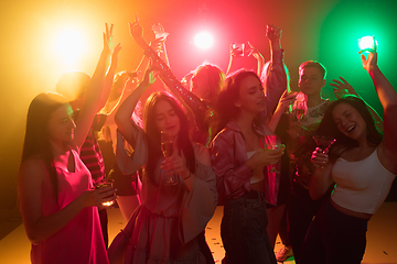 Image showing A crowd of people in silhouette raises their hands on dancefloor on neon light background