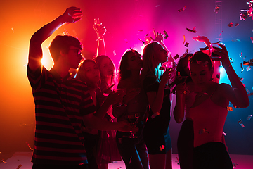 Image showing A crowd of people in silhouette raises their hands on dancefloor on neon light background