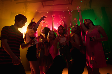 Image showing A crowd of people in silhouette raises their hands on dancefloor on neon light background