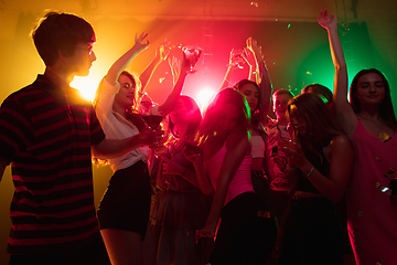 Image showing A crowd of people in silhouette raises their hands on dancefloor on neon light background