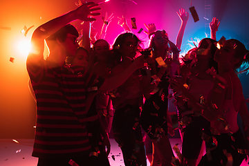 Image showing A crowd of people in silhouette raises their hands on dancefloor on neon light background