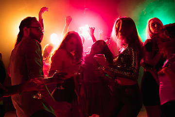 Image showing A crowd of people in silhouette raises their hands on dancefloor on neon light background