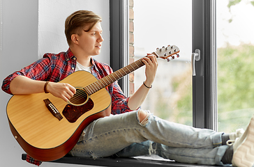 Image showing young man playing guitar sitting on windowsill