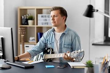 Image showing young man with computer playing guitar at home