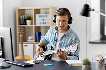 Image showing man in headphones playing bass guitar at home