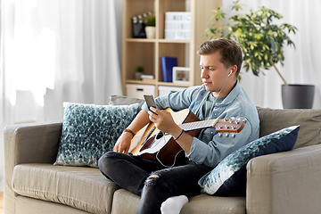 Image showing man with guitar, earphones and smartphone at home