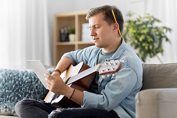 Image showing young man with guitar and music book at home