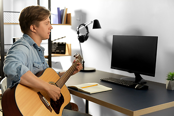 Image showing young man with computer playing guitar at home