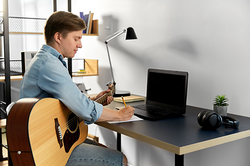 Image showing man with guitar writing to music book at home