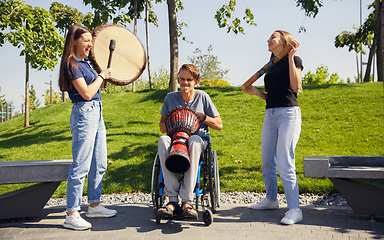 Image showing Happy handicapped man on a wheelchair spending time with friends playing live instrumental music outdoors