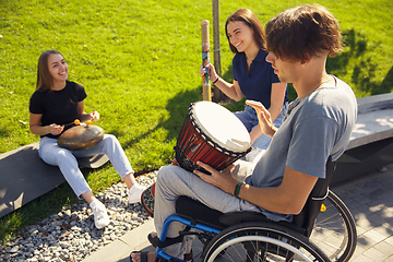 Image showing Happy handicapped man on a wheelchair spending time with friends playing live instrumental music outdoors
