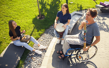 Image showing Happy handicapped man on a wheelchair spending time with friends playing live instrumental music outdoors