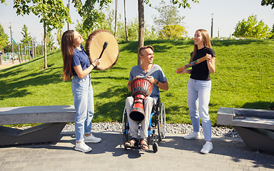 Image showing Happy handicapped man on a wheelchair spending time with friends playing live instrumental music outdoors