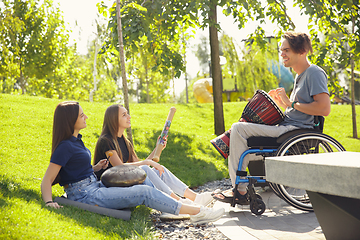 Image showing Happy handicapped man on a wheelchair spending time with friends playing live instrumental music outdoors