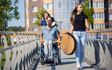 Image showing Happy handicapped man on a wheelchair spending time with friends playing live instrumental music outdoors