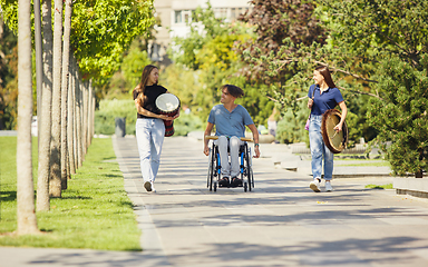 Image showing Happy handicapped man on a wheelchair spending time with friends playing live instrumental music outdoors