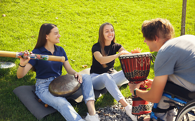 Image showing Happy handicapped man on a wheelchair spending time with friends playing live instrumental music outdoors